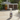 A white spray bottle of FERON SPAGARD Pool cleaner stands on a light stone patio in front of a blurred outdoor hot tub and potted plants.